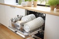 Dishwasher inside beautiful kitchen with white used dishes that prepared to wash. Housekeeping concept. Royalty Free Stock Photo