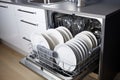 Dishwasher inside beautiful kitchen with white used dishes that prepared to wash. Housekeeping concept. Royalty Free Stock Photo