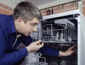 Dishwasher repair. A service center representative diagnoses and repairs a dishwashing machine at home. Specialist in working with Royalty Free Stock Photo