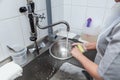 Dishwasher in uniform washes griddle with foam and sponge under the tap water Royalty Free Stock Photo