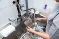 Dishwasher in uniform washes griddle with foam and sponge under the tap water