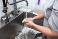 Dishwasher in uniform washes griddle with foam and sponge under the tap water