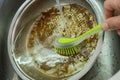 Dishwasher washing a dirty greasy frying pan with a brush in the washbasin