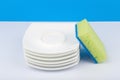 Dishwashing concept, high angle view of cleaning sponge and pile of clean saucers on white table with blue background