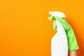 Disinfectant spray bottle mockup in female hand in green rubber glove over orange background. Kitchen cleaner product design Royalty Free Stock Photo