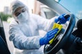 Disinfection professional cleans up a steering wheel of a car with a yellow rug. Sanitary service worker disinfects the vehicle`s