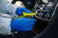 Disinfection professional wearing blue gloves cleans up an interior of a car with a yellow rug. Sanitary service worker disinfects