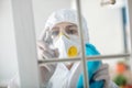 Woman in white workwear and respirator disinfecting the window