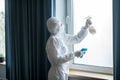 Woman in white workwear and respirator doing disinfection at home