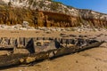 A carcass of a shipwreck on Old Hunstanton Beach in front of the white, red and orange stratified cliffs in Norfolk, UK