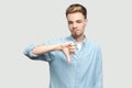 Dislike. Portrait of dissatisfied handsome young man in light blue shirt standing, thumbs down and looking at camera with sad face Royalty Free Stock Photo