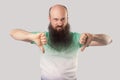 Dislike. Portrait of dissatisfied middle aged bald man with long beard in light green t-shirt standing thumbs down and looking Royalty Free Stock Photo