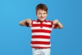 Little child boy in red striped shirt making disagree disapprove finger sign against blue background