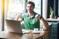 Dislike! Young dissatisfied businessman in green t-shirt sitting, working on laptop, looking at camera and showing thumbs down Royalty Free Stock Photo