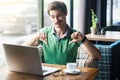 Dislike! Young dissatisfied businessman in green t-shirt sitting, working and looking at laptop screen and showing thumbs down Royalty Free Stock Photo