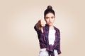 Dislike. Young unhappy upset girl with casual style and bun hair thumbs down her finger, on beige blank wall with copy space looki