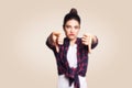 Dislike. Young unhappy upset girl with casual style and bun hair thumbs down her finger, on beige blank wall with copy space