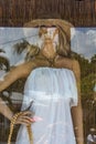 Display and reflection in Key West shop window of beautiful female manniquin with white dress and straw hat against bamboo curtain