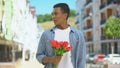 Displeased afro-american teen male with tulips angry about girlfriends lateness