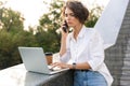 Displeased beautiful woman standing outdoors using laptop computer talking by phone Royalty Free Stock Photo