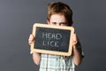 Displeased child hiding behind a school slate scaring head lice Royalty Free Stock Photo