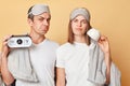 Displeased couple man and woman in sleep eye mask wrapped in blanket holding cup and alarm isolated over beige background waking Royalty Free Stock Photo