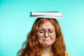 Portrait of frustrated teenage girl carrying book on head on blue