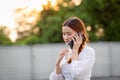 Displeased and disappointed girl with a mobile phone stands in parking lot . In the evening the sunset was orange. copy space