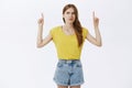 Displeased hesitant and bothered cute slim woman in yellow t-shirt and shorts raising hands pointing and looking up with Royalty Free Stock Photo