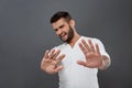 Displeased man refusing, stretching hands to camera over grey background.