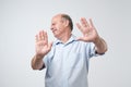 Displeased mature man refusing, stretching hands to camera over grey background.