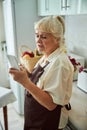 Displeased old woman using mobile phone in kitchen Royalty Free Stock Photo