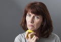 Displeased 50s woman thinking about skin aging with symbol of healthy lifestyle and fresh food in hand Royalty Free Stock Photo