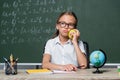 displeased schoolgirl holding apple near globe