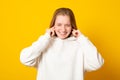 Displeased teen girl plugs ears with discontent, doesnt want to hear annoying sound or noise, dressed in white sweater Royalty Free Stock Photo