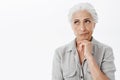 Displeased thoughtful and wise senior woman with gray hair smirking from dislike and irritationg thinking looking at Royalty Free Stock Photo