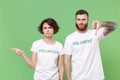 Displeased two friends couple in white volunteer t-shirt isolated on green background. Voluntary free work assistance