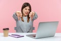 Displeased woman office worker showing thumbs down, dislike gesture, expressing disapproval, criticizing sitting at workplace with Royalty Free Stock Photo