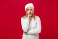 Displeased worried young woman in white sweater, hat isolated on red wall background, studio portrait. Healthy fashion Royalty Free Stock Photo