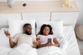 Displeased young african american guy gesturing, spreads hands, look at woman smartphone on bed Royalty Free Stock Photo