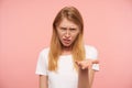 Displeased young attractive long haired redhead woman keeping her hand raised and frowning eyebrows while looking confusedly at