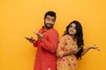 Indian couple arguing and gesturing while using mobile phones standing back to back isolated over yellow background Royalty Free Stock Photo