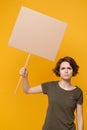 Displeased young protesting woman girl hold in hand protest sign broadsheet blank placard on stick isolated on yellow Royalty Free Stock Photo