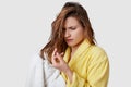 Displeased young woman realizes she has damaged hair, looks stressfully at ends, being wet after taking shower, wipes with white Royalty Free Stock Photo