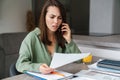 Displeased young woman talking on mobile phone while working with papers Royalty Free Stock Photo