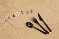 Disposable black appliances fork, spoon, knife, inscription Plastic from letters on transparent base on brown crumpled craft paper