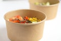 Disposable cardboard plate with a bowl of fresh vegetables and shrimp based on bulgur on a white background. Diet food.