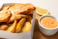 Disposable container with British Traditional Fish and potato chips on wooden board Royalty Free Stock Photo