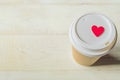 Disposable craft paper coffee cup and red wooden heart on a cap. Coff to go on wooden table Royalty Free Stock Photo