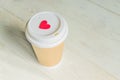 Disposable craft paper coffee cup and red wooden heart on a cap. Coff to go on wooden table Royalty Free Stock Photo